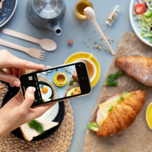 weibliche Hände halten Smartphone und fotographieren Frühstück mit Croissants und Gemüse