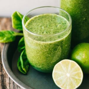 Ein kleines Tablett auf dem eine Glasflache mit einem grünen Smoothie darin steht, daneben ein kleines Glas, das ebenfalls mit dem grünen Smoothie befüllt ist