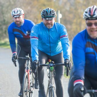 Drei Herren mittleren Alters fahren gemeinsam föhlich Rennrad in der Natur