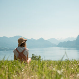 Frau sitzt entspannt im Feld neben einem See, die Sonne scheint.