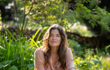 Frau mit braunen Haaren sitzt in ihrem grünen Garten im Sommer.