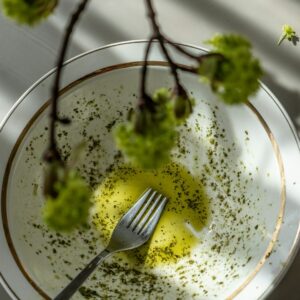 Auf einem weißen Teller ist etwas Kräuteröl, darüber ragt ein Ast.