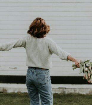 Frau mit Blumen in der Hand hat ihre Arme ausgebreitet und dreht sich.