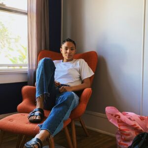 Eine Frau sitzt auf einem Sessel und guckt Selbstbewusst in die Kamera.