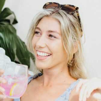 Eine junge lachende Frau hält ein Glas Limonade in der Hand.