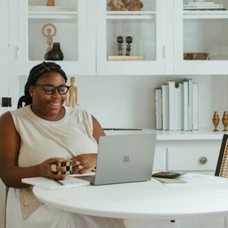 Eine plus size Frau sitzt an einem Tisch vor ihrem Laptop.