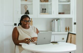 Eine plus size Frau sitzt an einem Tisch vor ihrem Laptop.