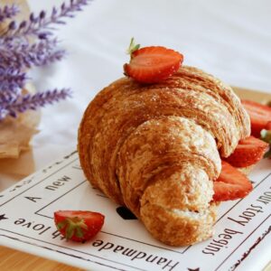 Croissant mit Erdbeeren getoppt auf einem Schneidebrett.
