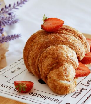 Croissant mit Erdbeeren getoppt auf einem Schneidebrett.