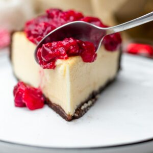 Ein Stück Käsekuchen mit Himbeeren und Soße.