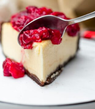 Ein Stück Käsekuchen mit Himbeeren und Soße.