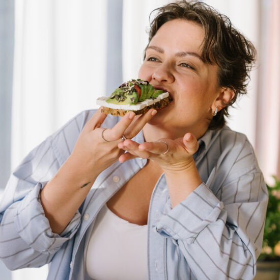 Frau isst ein belegtes Vollkornbrot mit Avocado, Tomaten und Frischkäse.