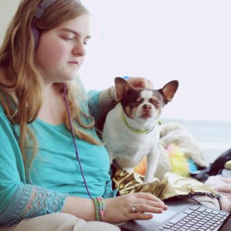Übergewichtige Frau sitzt auf einem Sofa mit ihrem Hund und arbeitet am Laptop.