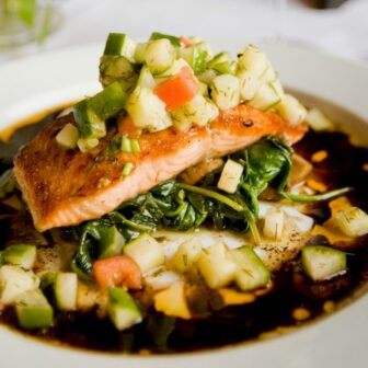Lachs mit Gemüse und Soße auf einem Teller garniert.