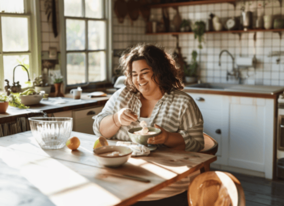 Eine plus size rau sitzt ein ihrer Küche und isst eine Joghurt Bowl.