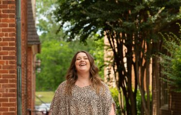 Eine plus size Frau geht spazieren und schaut glücklich in die Kamera.