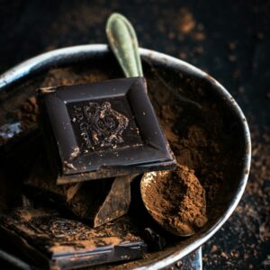 Ein Stück dunkle Schokolade auf einem Teller mit Kakaopulver.