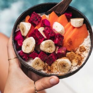 Eine Hand hält eine Porridge Bowl mit frischem Obst. Im Hintergrund sieht man einen swimming pool.