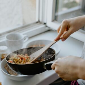 Ein Ausschnitt, auf dem gerade ein Linsengericht aus einer Pfanne auf einen Teller serviert wird.