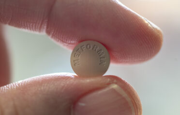 Eine Tablette Metformin klemmt zwischen zwei Fingern.