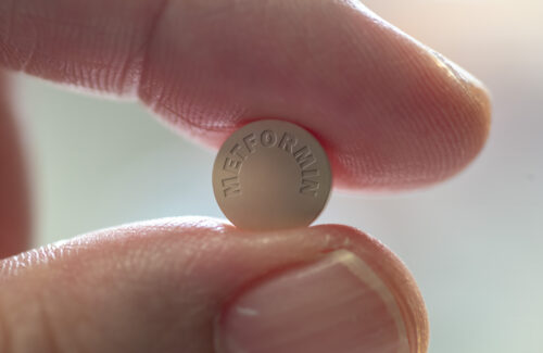 Eine Tablette Metformin klemmt zwischen zwei Fingern.