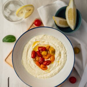 Eine Schüssel mit frischem Hummus einem Schuss Olivenöl und Tomaten.