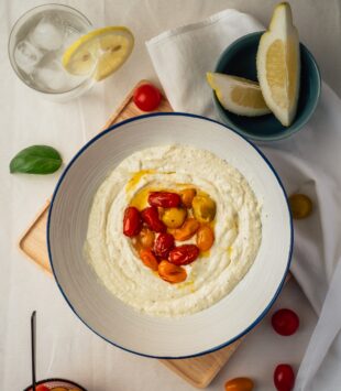 Eine Schüssel mit frischem Hummus einem Schuss Olivenöl und Tomaten.