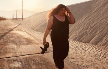 Eine junge plus size Frau geht im Sonnenuntergang einen Sanweg entlang.