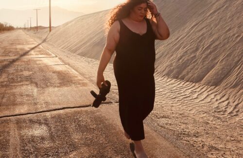 Eine junge plus size Frau geht im Sonnenuntergang einen Sanweg entlang.