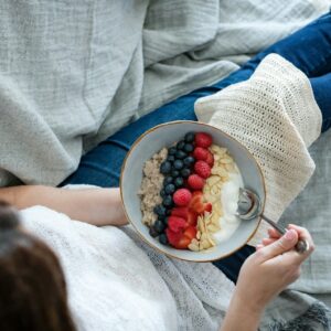 Eine Person hält auf ihrem Schoß eine Jogurt Bowl mit Haferflocken und Beeren.