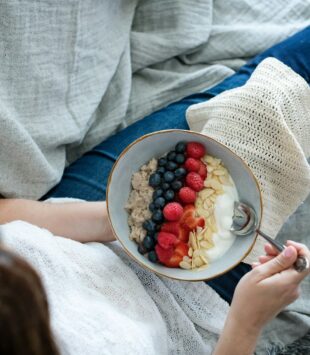 Eine Person hält auf ihrem Schoß eine Jogurt Bowl mit Haferflocken und Beeren.