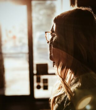 Eine junge Frau sieht nachdenklich aus dem Fenster.