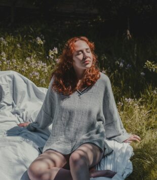 Eine junge Frau sitzt auf einer Picknick Decke in der Sonne und hält hr Gesicht genussvoll Richtung Sonne.