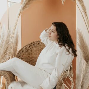 Eine junge Frau sitzt gemütlich auf einem Sessel und schaut zur Seite.