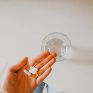 Eine Hand hält ein paar Tabletten, daneben steht ein Wasserglas.