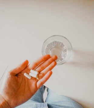 Eine Hand hält ein paar Tabletten, daneben steht ein Wasserglas.
