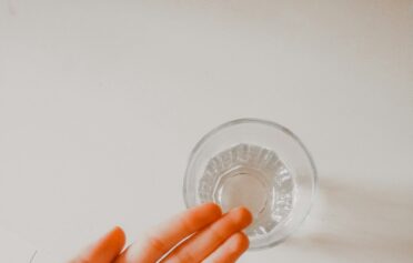 Eine Hand hält ein paar Tabletten, daneben steht ein Wasserglas.