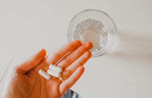 Eine Hand hält ein paar Tabletten, daneben steht ein Wasserglas.