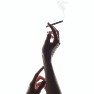 Eine Auschnitt einer Hand, die eine rauchende Zigarette in der Hand hält.