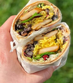 Eine Hand hält zwei Hälften von einem gesunden Wrap in die Kamera.