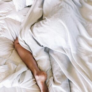 Eine Person liegt schlafend im Bett und ist bedeckt mit der Bettdecke, nur ein Bein guckt heraus.