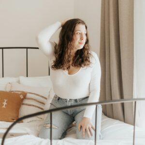 Eine junge Frau kniet auf einem Bett und blickt aus dem Fenster.