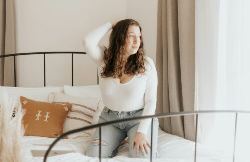 Eine junge Frau kniet auf einem Bett und blickt aus dem Fenster.