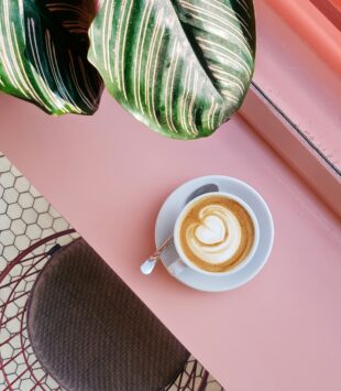 Eine Tasse Cappucino auf einem rosa Tisch im Cafe.