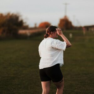 Eine plus size Frau spaziert über eine Wiese und blickt in die Ferne.