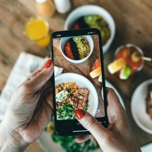 Ein Auschnitt, auf dem zu sehen ist, wie jemand ein Bild von seinem gesunden Essen mit einem Smartphone macht.