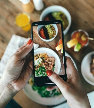 Ein Auschnitt, auf dem zu sehen ist, wie jemand ein Bild von seinem gesunden Essen mit einem Smartphone macht.