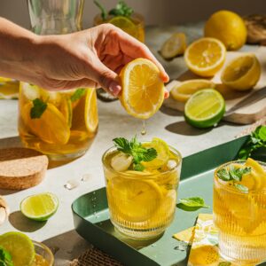 Zwei Gläser mit Zitronenlimonado, wo in ein Glas noch extra Zitronensaft gequetscht wird.