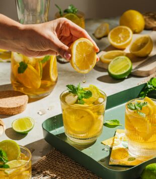 Zwei Gläser mit Zitronenlimonado, wo in ein Glas noch extra Zitronensaft gequetscht wird.