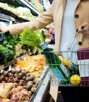 Ein Ausschnitt von einer Person im Supermarkt, die ihren Korb mit Gemüse und gesunden Lebensmitteln füllt.